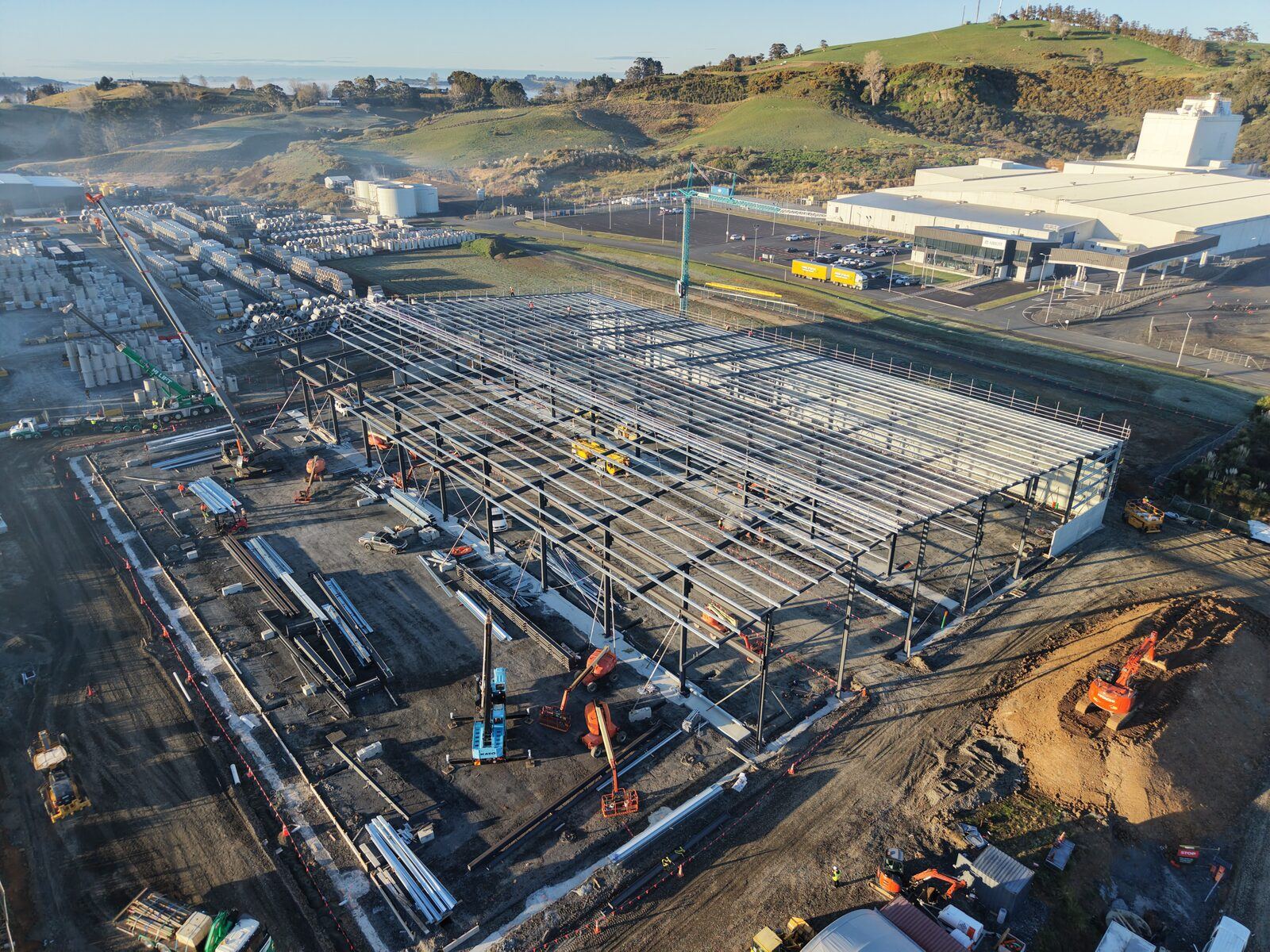 Close aerial of cranes and crew working along the roof purlins at Hynds Pōkeno